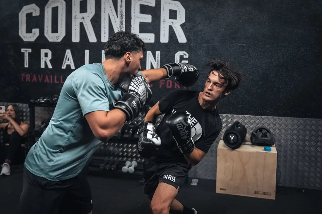 Deux boxeurs à l'entraînement devant le logo Corner Training peint sur le mur de la salle
